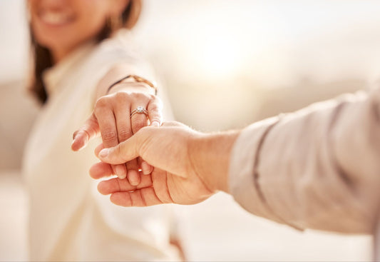 Close-up of a sparkling moissanite engagement ring on a woman’s hand as she reaches for her fiancé.